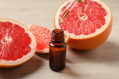 Pipetten şişeye akan greyfurt yağı ve açık ahşap masada taze meyveler.