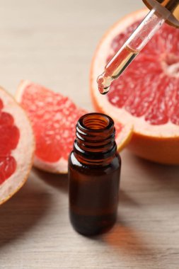Pipetten şişeye akan greyfurt yağı ve açık ahşap masada taze meyveler.