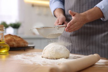 Ekmek yapıyorum. Mutfaktaki ahşap masada hamura un serpiştiren adam.