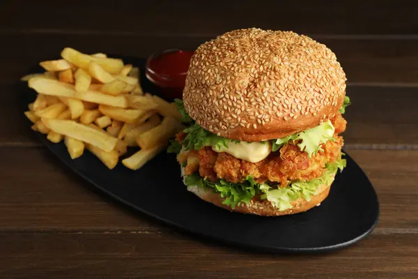 Delicious burger with crispy chicken patty, french fries and sauce on wooden table