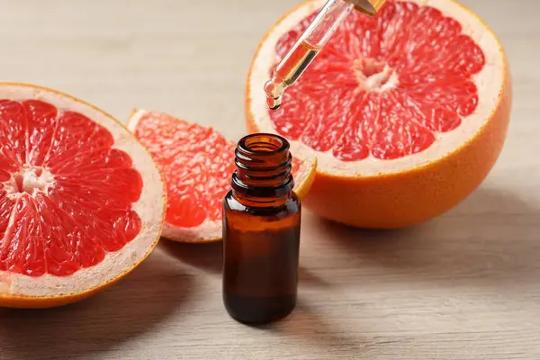Pipetten şişeye akan greyfurt yağı ve açık ahşap masada taze meyveler.