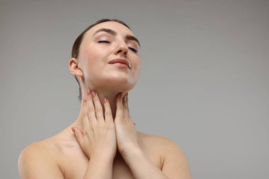 Gri arka planda boynuna dokunan güzel bir kadın. Metin için boşluk