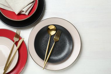 Beyaz ahşap masaya seramik tabaklar, çatal bıçak takımı ve peçete.