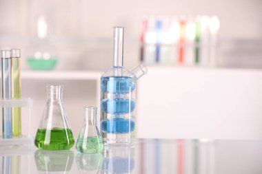 Laboratuvar analizi. Kapalı alandaki beyaz masa üzerinde sıvı bulunan farklı cam eşyalar. Metin için boşluk