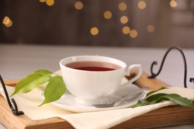 Fincanda romatik çay, çay tabağı, kaşık ve yeşil yapraklar masada.
