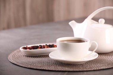 Fincanda romatik çay, çay tabağı, çaydanlık ve gri masada kuru çiçek yaprakları.