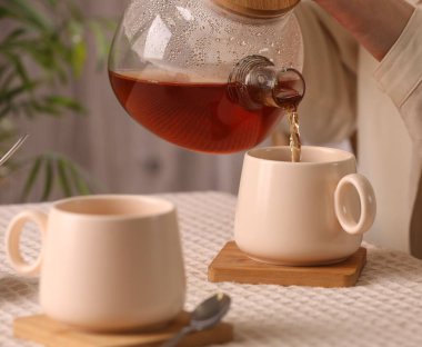 Kadın masadaki fincana aromatik çay dolduruyor, yakın plan.