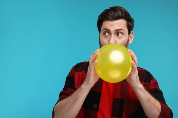 Man inflating yellow balloon on light blue background. Space for text