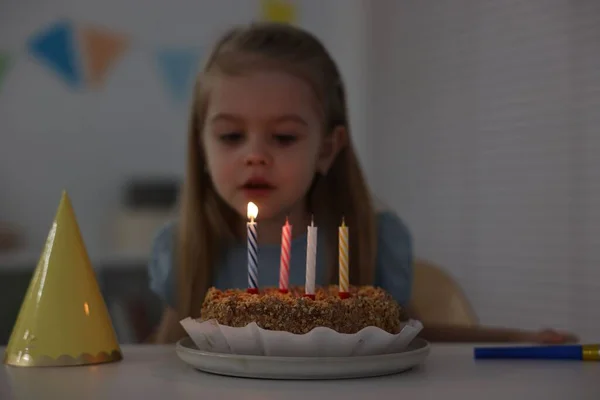 Cute girl with birthday cake at table indoors, focus on candles