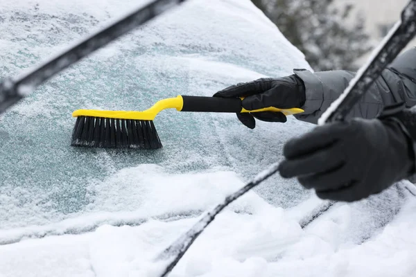 Arabanın ön camından kar temizleyen adam, yakın plan.