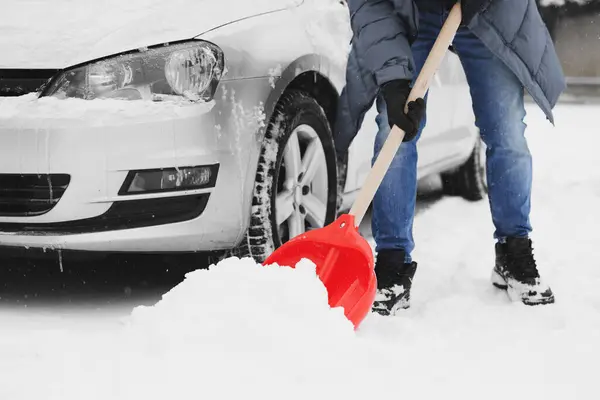 Adam arabanın yanında kürekle karları kaldırıyor, yakın plan.