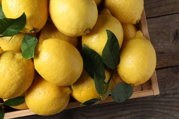 Tahta masadaki sandıkta taze limonlar ve yeşil yapraklar.