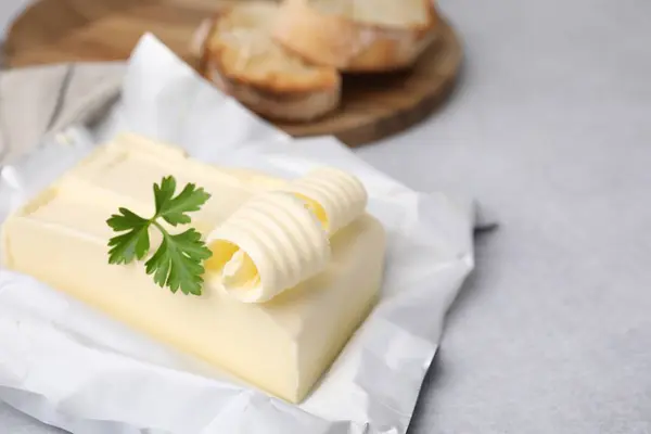 Tasty butter with curl and parsley on light grey table, closeup. Space for text