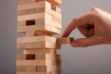 Jenga oynuyorum. Gri arkaplandaki tahta bloğu kuleden kaldıran adam, yakın plan
