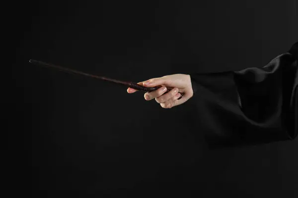 Wizard holding magic wand on black background, closeup