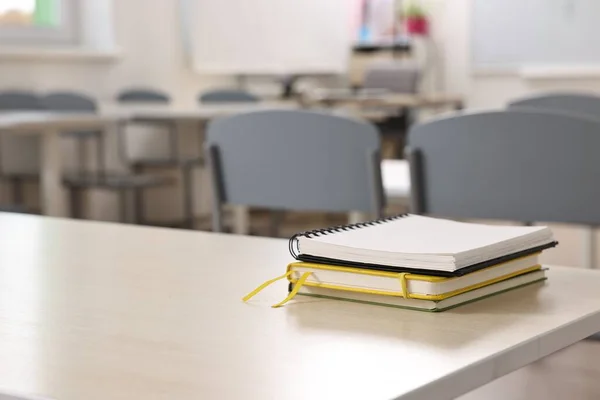 Stack of notebooks on wooden desk in empty classroom