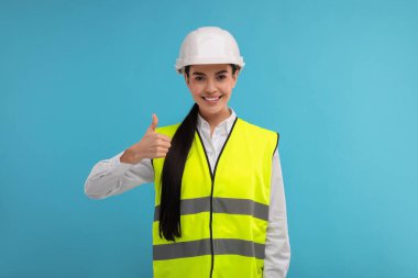 Açık mavi arka planda baş parmağını gösteren sert şapkalı bir mühendis.