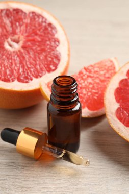 Bir şişe greyfurt yağı ve hafif ahşap masada taze meyveler.