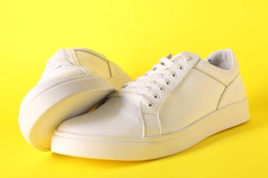 Sarı arka planda bir çift şık beyaz spor ayakkabı.