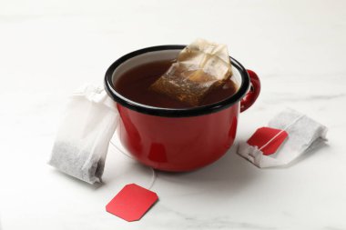 Çay poşetleri ve bir fincan sıcak içecek beyaz masada, yakın plan.