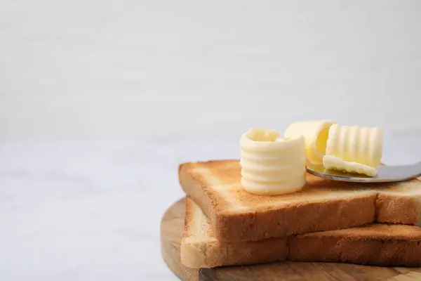 Tasty butter curls, knife and toasts on white table, closeup. Space for text