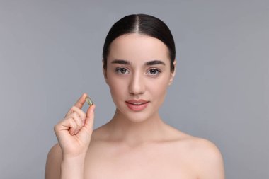 Gri arka planda vitamin hapı olan güzel bir genç kadın.