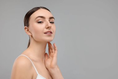 Gri arka planda boynuna dokunan güzel bir kadın. Metin için boşluk