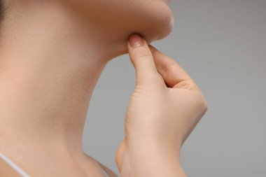 Gri arka planda çenesine dokunan kadın, yakın plan.