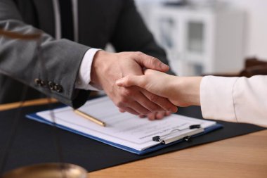 Ofisteki ahşap masada müşteriyle tokalaşan noter, yakın plan.