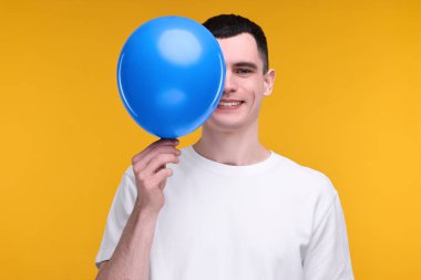 Sarı arka planda açık mavi balonu olan mutlu genç adam.