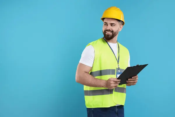 Engineer in hard hat holding clipboard on light blue background, space for text
