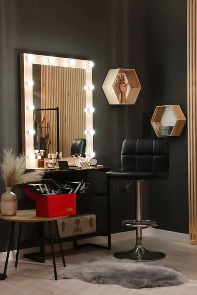 Makeup room. Stylish mirror near dressing table with beauty products and chair indoors