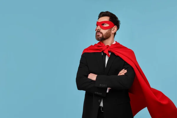Businessman wearing red superhero cape and mask on light blue background. Space for text