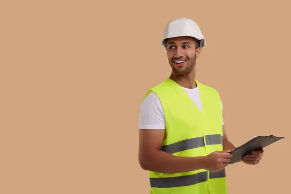 Engineer in hard hat holding clipboard on beige background, space for text
