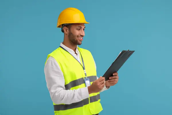 Engineer in hard hat holding clipboard on light blue background