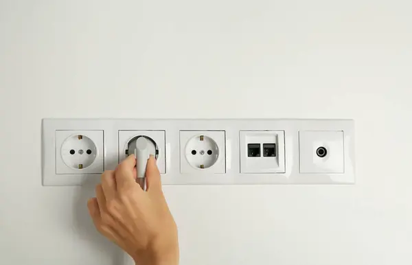 Woman putting plug into socket indoors, closeup