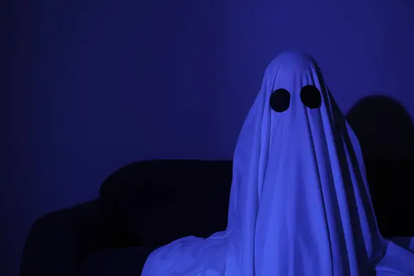 Creepy ghost. Woman covered with sheet in blue light, space for text