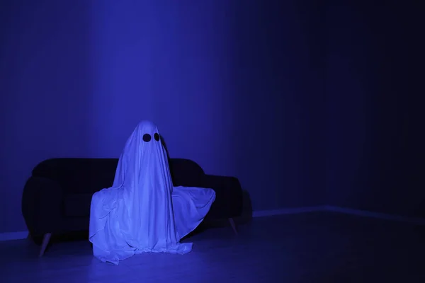 Creepy ghost. Woman covered with sheet sitting on sofa in blue light, space for text