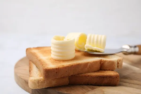 Tasty butter curls, knife and toasts on white table, closeup