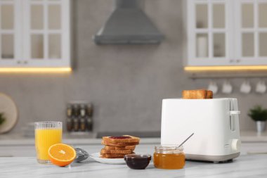 Kahvaltı için kadeh kaldırıyorum. Cihaz, çıtır ekmek, bal, reçel ve portakal. Mutfaktaki beyaz masada taze.