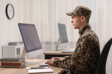 Askerlik. Ofisteki tahta masada bilgisayarla çalışan genç asker.