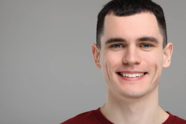 Temiz dişleri olan yakışıklı genç adam gri arka planda gülümsüyor, mesaj için yer var.