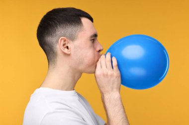 Sarı arka planda açık mavi balon şişiren genç adam