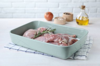 Beyaz ahşap masada çiğ tavşan eti ve biberiye.