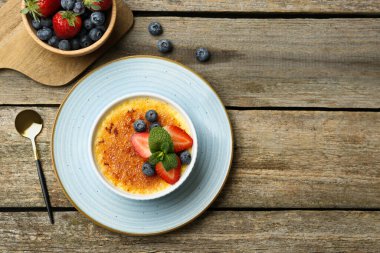 Böğürtlenli ve nane şekerli nefis creme brulee, ahşap masada servis edilir, düz yatar. Metin için boşluk