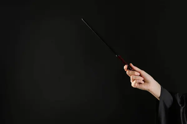 Wizard holding magic wand on black background, closeup. Space for text