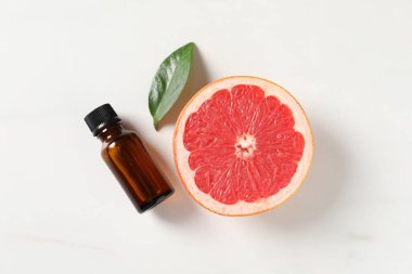 Şişede greyfurt yağı, beyaz masada yaprak ve meyve, düz uzanmış.
