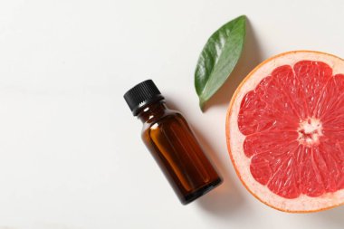 Şişede greyfurt yağı, beyaz masada yaprak ve meyve düz yerde. Metin için boşluk