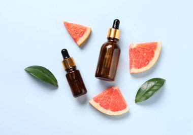 Şişelerde greyfurt yağı, yapraklar ve açık mavi masa üzerinde meyve kesme, düz uzanma