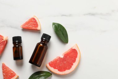 Şişelerde greyfurt yağı, yapraklar ve beyaz mermer masa üzerinde meyve kesimi. Metin için boşluk